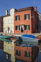Moored boats on canal lined with red and yellow stucco houses, Burano Island, Venetian Lagoon,