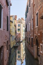 Narrow canal with moored boats and old architectural style stucco and brick residential buildings,