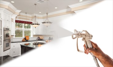 Professional spray painter holding spray gun spraying new renovated kitchen over white surface