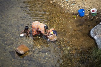 Indian woman washing clothes in the Periyar River, her son playing next to her, Mundakayam, Kerala,