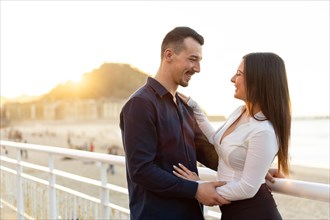 Young elegant couple embracing looking each other during sunset next to the beach