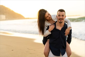 Woman piggybacking her boyfriend on the beach during sunset