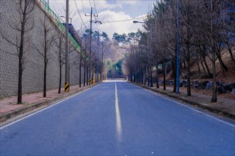 Empty tree lined street in industrial park on winter morning under partly cloudy sky in South Korea