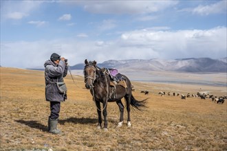 Nomadic life on a plateau, shepherd on horse, flock of sheep, dramatic high mountains, Tian Shan