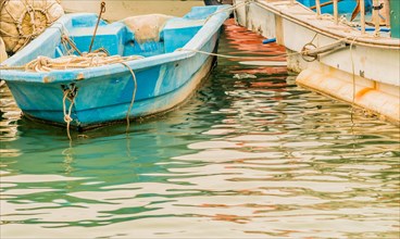 Closeup of small blue fishing boat floating in water tied to a larger white fishing boat in South