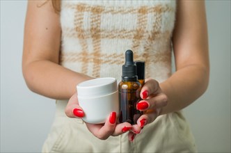 Young woman holding and showing with her hands set of skin care products, serum, creams, personal