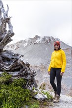 Young woman in yellow jacket standing in front of a volcano, Chaiten Volcano, Carretara Austral,