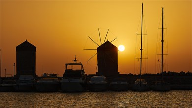 Harbour view with windmills and boat silhouettes at a bright sunrise, twilight, Mandraki Harbour,