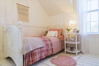 Single bed with red, pink and grey tartan bedspread, white painted antique style wooden headboard