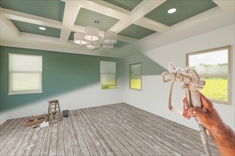 Professional spray painter holding spray gun spraying renovated room over unfinished room