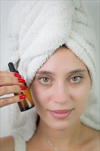 Happy young woman with towel on head holding amber glass bottle of skin serum. Beautiful young
