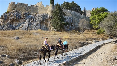 Donkey trail to the Acropolis, children riding donkeys on a dusty hiking trail in front of an old