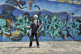 A ten-year-old boy plays with his football in front of a graffiti wall, Germany, Europe