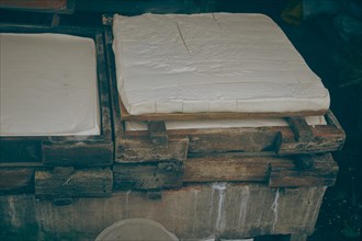 Overhead view of soy curd being pressed into wooden mold in a traditional Indonesian tahu or tofu