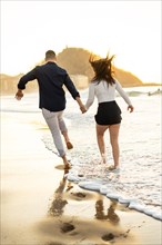 Vertical rear view photo of a caucasian elegant young free young couple running barefoot on the