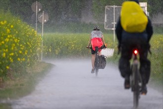 Two cyclists riding along a country lane in heavy rain in the north-west of Frankfurt am Main,