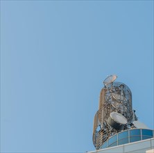 Large circular communication tower on roof of modern building with blue sky in background in South