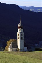 Small church with white tower in front of wooded hills and blue sky, Italy, Trentino-Alto Adige,