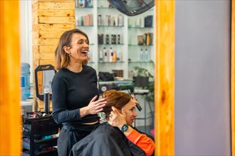 Reflection view on a mirror of a hairdresser laughing while talking and combing a female customer