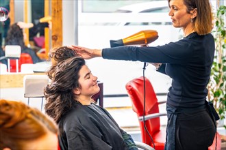 Side view of a beauty hairdresser drying the hair of a woman using hairdryer in the salon