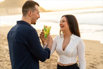 Romantic toast of a young caucasian elegant couple standing on the beach during sunset