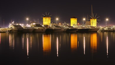 Oat at night with illuminated windmills and yachts reflected in the water, twilight, Mandraki