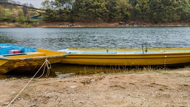 Two yellow metal boats tied up at the shore of a peaceful lake with trees on the far shoreline in