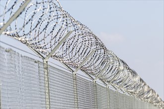 A security fence with barbed wire in front of a clear blue sky