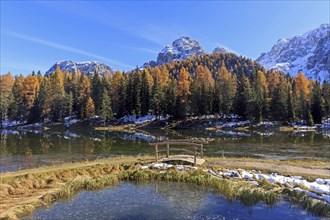 Autumn mountain landscape with a bridge over a clear lake and snow-covered peaks, Italy, South