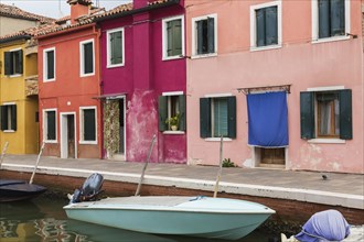 Moored boats in canal lined with pink, purple, red and yellow stucco houses decorated with curtains