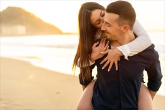 Horizontal photo with copy space of a couple kissing and piggybacking during sunset on the beach
