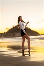 Vertical portrait of an elegant beauty woman posing sensual on the beach during sunset