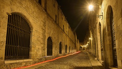 Quiet old stone street at night with warm lights leaving a harmonious impression, red light trail,