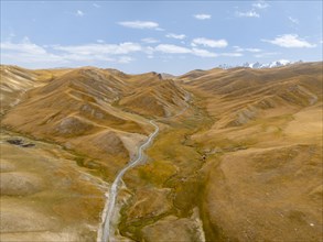 Aerial view, road winds through a mountain valley with hills of yellow grass, Naryn Province,