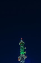Low angle night view of large communication array tower lit up in red lights with dark blue sky in