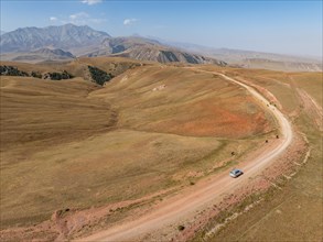 Moldo-Ashuu Pass, car on road between yellow hills, near Baetov, Naryn region, Kyrgyzstan, Asia