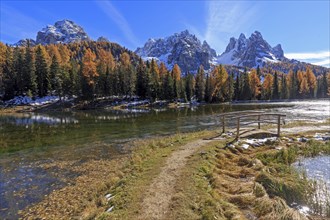 A hiking trail leads to a quiet lake surrounded by autumnal trees and mountains, Italy, South