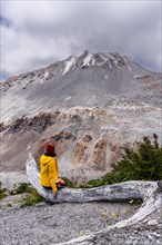 Young woman in yellow jacket sits in front of a volcano, Chaiten Volcano, Carretara Austral, Chile,