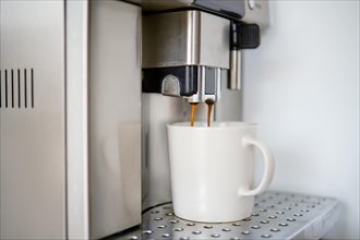 Coffee is poured into a cup from a coffee machine, closeup view