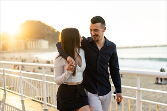 Romantic couple embracing looking at each other walking along a promenade during sunset