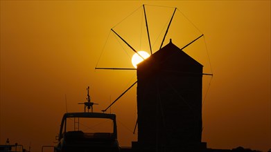 Silhouette of a windmill against the background of an orange sunrise sky, twilight, Mandraki Oat,