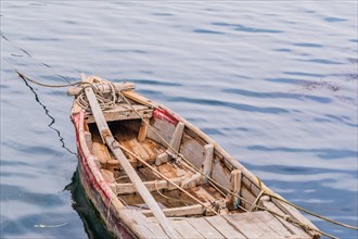Small wooden rowboat with floating in calm water with ropes leading to the shore in NamHae, South