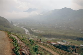 A misty view of a village in a valley with a river flowing through, surrounded by mountains in Lao