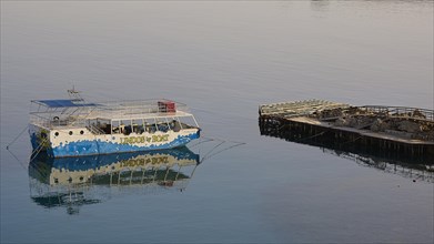 An excursion boat is reflected in the calm waters next to a wooden jetty, Lindos, Rhodes,