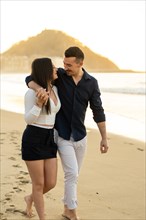 Vertical photo of a young chic romantic couple enjoying sunset walking along a beach
