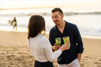 Horizontal photo of a young happy couple toasting during sunset on the beach