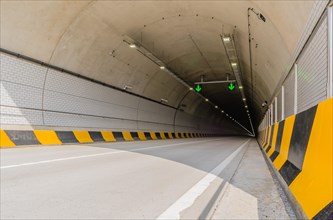 Two lane highway tunnel of white concrete with florescent lights and green arrows on ceiling and