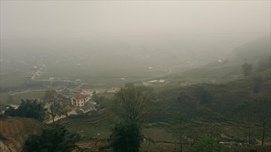 A foggy rural landscape with terraced fields and a singular house amidst greenery in Lao Cai
