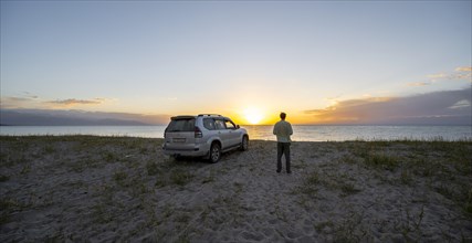 Tourist with off-road vehicle Toyota Land Cruiser at Issyk Kul Lake at sunset, Issyk Kul,