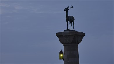 Deer statue on column with illuminated lantern at dusk, Mandraki Oat, Rhodes, Dodecanese, Greek